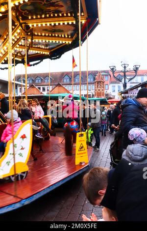 Hanau, Deutschland - 15. Dezember 2019: Kinder auf einem Karussell und Menschen auf Gehwegen auf einem Weihnachtsmarkt in Hanau. Stockfoto