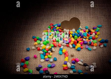 Herz aus Papier inmitten der bunten Steinchen auf Leinwand Boden Stockfoto