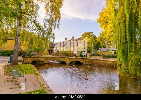 Bourton-on-the-Water, Großbritannien - 17. Oktober 2022: Sonnenuntergang mit typischen Häusern, dem Fluss Windrush, Einheimischen und Besuchern im Dorf Bourton-on-the-Wa Stockfoto