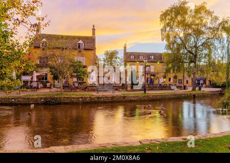 Bourton-on-the-Water, Großbritannien - 17. Oktober 2022: Sonnenuntergang mit typischen Häusern, dem Fluss Windrush, Einheimischen und Besuchern im Dorf Bourton-on-the-Wa Stockfoto