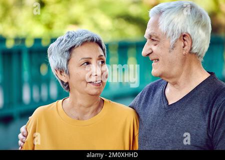 Optimistisch attraktive, multiethnische ältere 60s sportliche Paare posieren im Park und schauen einander mit Zärtlichkeit und Liebe an. Glückliche Ehe Stockfoto