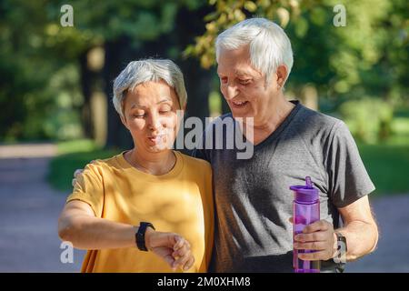 Gealtertes Paar trainieren im Sommerpark tragen watch Check Daten mit Anwendung Pflege über Gesundheit. Sportlich aktiv im Ruhestand Ehepartner Lebensstil mit modernen Stockfoto