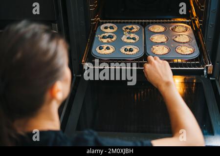 Frauenhände, die ungekochte Muffins mit Blaubeeren in die Küche legen. Ein junges erwachsenes Mädchen, das zu Hause Gebäck kocht. Stockfoto