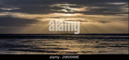 Sonnenstrahlen durch eine Lücke in den Wolken - am späten Nachmittag auf leeren Schlammflächen. Stockfoto