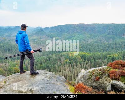 Fotograf mit gefaltetem Stativ am Ende des Klippendenkens. Natürliche Waldlandschaft im wunderschönen Tal Stockfoto