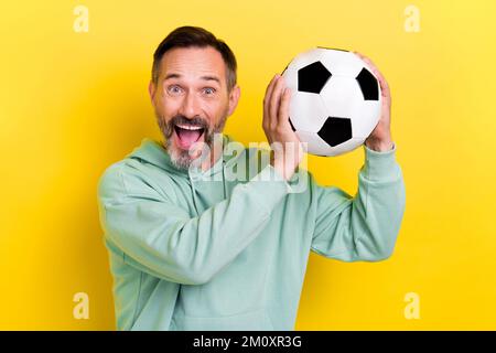 Portrait eines zufriedenen, aufgeregten, fröhlichen Mannes strahlende Hände halten den Ball isoliert auf gelbem Hintergrund Stockfoto