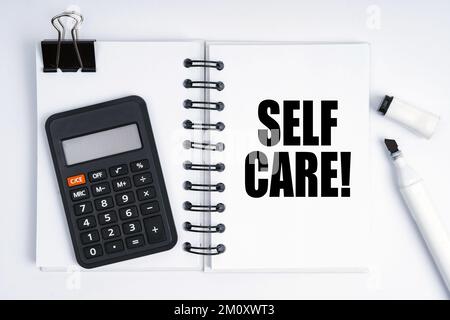 Wirtschafts- und Finanzkonzept. Auf dem Tisch befinden sich ein Marker, ein Taschenrechner und ein Notizbuch mit der Aufschrift „Self Care“ Stockfoto