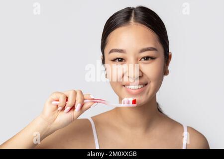 Lächelnde Frau mit weißen Zähnen, die Zahnbürste mit Zahnpasta auf weißem Hintergrund hält Stockfoto