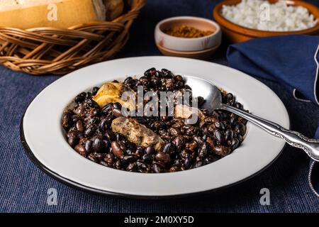 Bohnen und Schweinefleisch, auf weißem Teller mit Löffel. Typisch brasilianisches Essen. Stockfoto