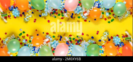 Geburtstagshintergrund, Draufsicht. Ballons und verschiedene Partydekorationen auf gelbem Hintergrund Stockfoto