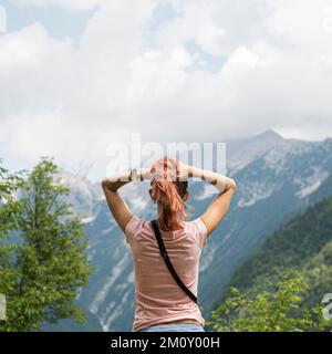 Blick von hinten auf eine junge Frau, die die wunderschöne Natur mit Blick auf die Berge genießt. Stockfoto