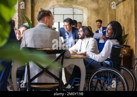 Multiethnische Teamarbeit mit einem großen Meeting für die Planung von Geschäften, afrikanische Frau im Rollstuhl, die mit Kollegen diskutiert Stockfoto