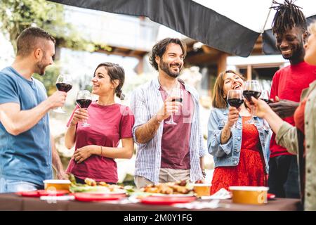 Gruppe glücklicher Freunde, die Spaß haben, während sie Rotwein trinken und Essen auf der Party essen, konzentrieren sich auf junge, gutaussehende Männer, echte Menschen Stockfoto