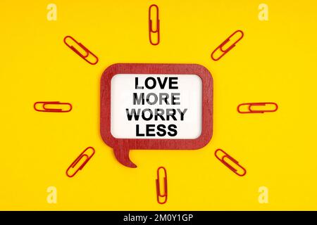 Menschen- und Naturbegriff. Auf gelbem Hintergrund, Büroklammern und einer mentalen Tafel mit der Aufschrift „Love More Worry Less“ Stockfoto