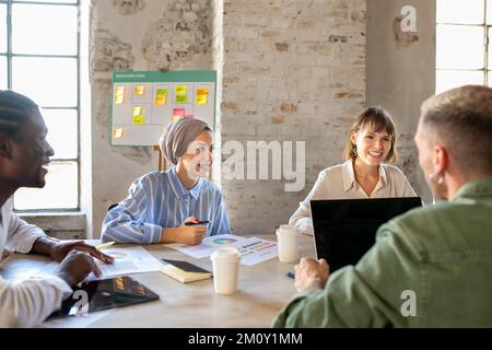 Ein junges, multiethnisches Team kreativer Kollegen, die in einem offenen Raum arbeiten, eine muslimische Geschäftsfrau mit ihrer Teamarbeit als kreative und Modedesignerin Stockfoto