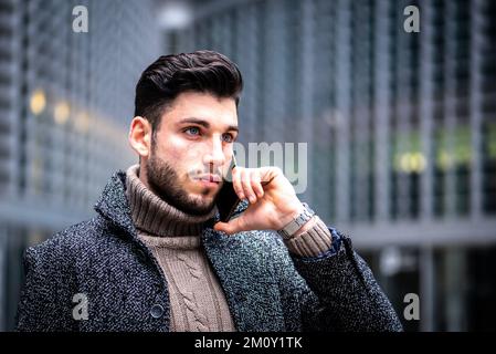 Porträt eines jungen Mannes mit intensiv aussehendem, modernem Geschäftsmann, der ein Smartphone für die Arbeit benutzt, männliches Model mit blu-Augen, dunklem Haar und kurzem Bart, CO Stockfoto
