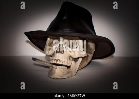 Ein Skelettschädel, der einen Lederhut trägt, raucht einen Marihuana-Joint Stockfoto