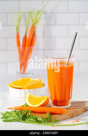 Frischer Bio-Karotten-Orangensaft mit Orangenscheiben in einer hellen Küchenumgebung mit Kopierbereich Stockfoto