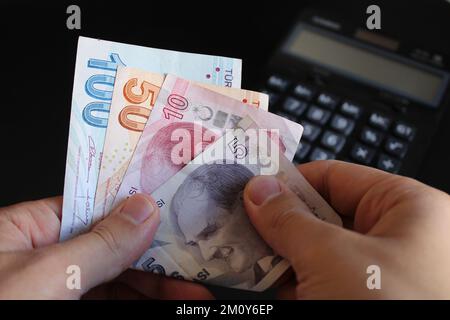 Ein Mann, der türkisches Geld mit der Hand zählt. Türkische Lira-Banknoten. Die Papierwährung der Türkei.Calculator im Hintergrund. Für Steuern und Wandernachrichten. Stockfoto