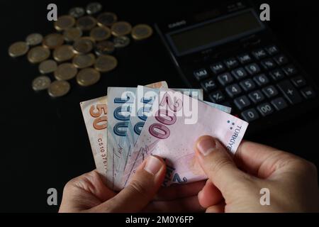 Ein Mann, der türkisches Geld mit der Hand zählt. Türkische Lira-Banknoten. Die Papierwährung der Türkei.Calculator im Hintergrund. Für Steuern und Wandernachrichten. Stockfoto