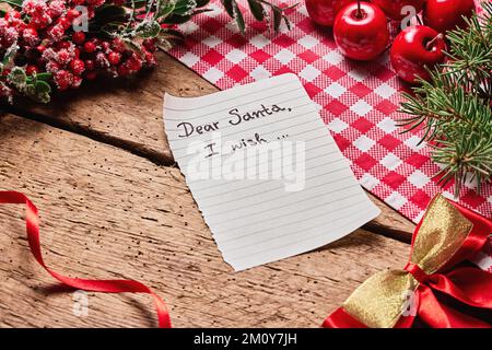 Lieber Weihnachtsmann Wunschkarte und Brief auf Holzschreibtisch mit vielen bunten Weihnachtsdekorationen und Neujahrsdekoration Stockfoto