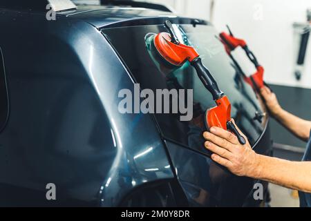 Nahaufnahme eines nicht erkennbaren Kaukasiers mit Saugnäpfen für Autofenster, um die Heckscheibe aus dem schwarzen Auto zu entfernen. Hochwertiges Foto Stockfoto