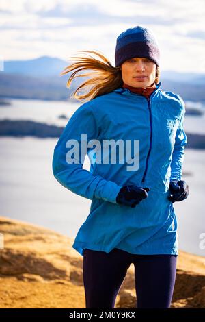 Eine Frau rennt in den Bergen mit einem See hinten Stockfoto