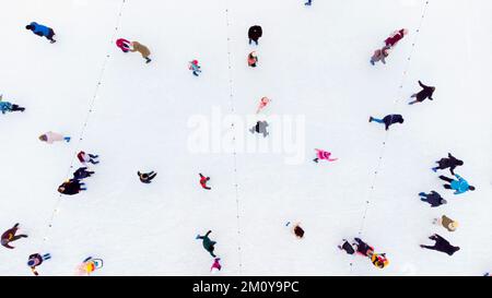 Leute, die auf einer Freiluft-Eislaufbahn skaten. Draufsicht. Viele Leute laufen auf der Eisbahn. Drohnenansicht Aus Der Vogelperspektive. Schöner Hintergrund für Skating-Sport und Winteraktivitäten im Freien Stockfoto