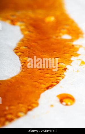 Medizinisches Cannabiswachs, das auf dem Papier herunterläuft, Orangenblasen Harz Marihuana. Stockfoto