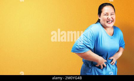 Asiatische, fettübergewichtige Frau, die Magenschmerzen mit farbigem Hintergrund hat Stockfoto