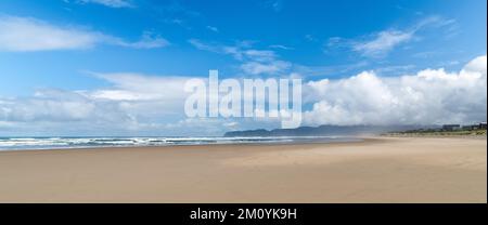 Panoramablick auf einen großen Sandstrand gesäumt mit Ferienhäusern unter blauem Himmel mit weißen Sturmwolken - McPhillips Beach, Oregon Stockfoto