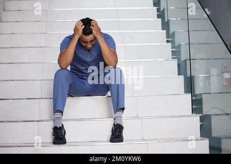 Ich fühle mich, als würde ich den Verstand verlieren. Ein junger männlicher Arzt, der weint, während er in einem modernen Krankenhaus arbeitet. Stockfoto