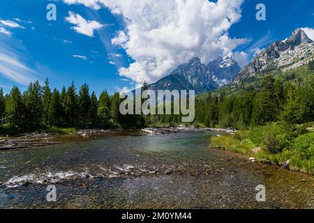 Im Grand Teton National Park, Wyoming, fließt ein breiter Fluss durch Kiefernwälder zu hohen Berggipfeln unter einem dramatischen, stürmischen Himmel Stockfoto