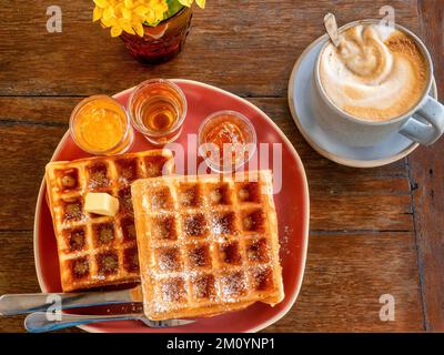 Blick von oben auf ein köstliches süßes Frühstück mit belgischen Waffeln und Kaffee, serviert auf einem rustikalen Holztisch. Stockfoto