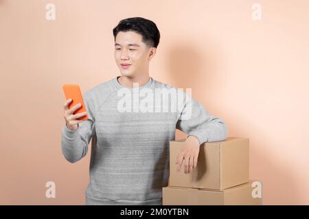 Asiatischer männlicher Geschäftsführer, der die Paketkartons per Handy überprüft. Stockfoto