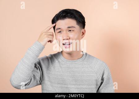 Junger asiatischer Mann, der unglücklich auf die Stirn zeigt, Stockfoto