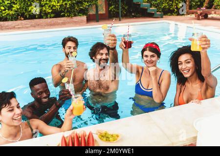 Millennial multiethnische Freunde feiern auf der Poolparty, indem sie Fruchtsaft, Cocktails, Gläser und Spaß sammeln - junge Leute toasten Stockfoto