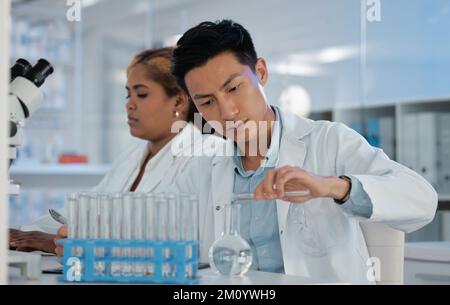 Er strebt nach Perfektion. Ein junger Labortechniker, der Flüssigkeit in einen Behälter gießt. Stockfoto