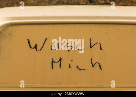 Die deutschen Wörter 'wasch mich' (Wasch mich) stehen auf einem dreckigen (orangefarbenen Sand) Fenster eines Autos Stockfoto