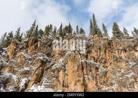 Winterlandschaft mit schneebedeckten Bäumen auf farbenfrohen Klippen unter einem stürmischen Himmel in den Jemez Mountains, New Mexico Stockfoto