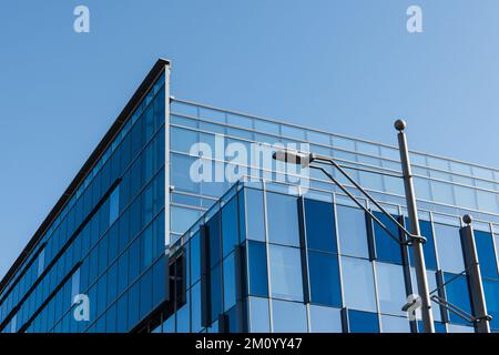 Schräge Aussicht auf ein modernes Glas-Stahl-Gebäude mit blauem Farbschema unter einem perfekten blauen Himmel Stockfoto