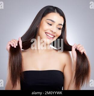 Mein Haar fühlt sich stärker und voluminöser an als je zuvor. Studioaufnahme einer attraktiven jungen Frau, die ihr Haar vor grauem Hintergrund bürstet. Stockfoto