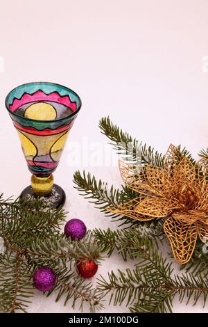 Neues Jahr. Buntes handgemachtes Glas auf dem Hintergrund von Fichtenzweigen mit glänzenden Kugeln und einer goldenen Blume. Vertikales Format. Stillleben. Stockfoto