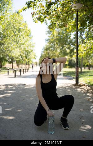 Lächelnde Sportlerin, die im Park auf dem Skateboard sitzt Stockfoto