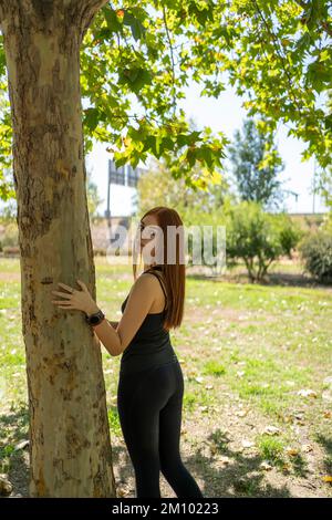 Schlanke Frau in Sportbekleidung, die sich an einen Baum lehnt Stockfoto