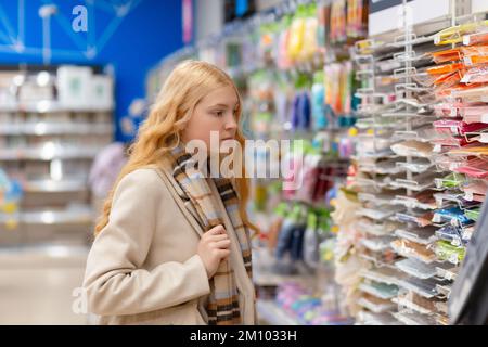 Porträt einer jungen Frau, die Schulpapier in einem Fachgeschäft auswählt. Mädchen, die Cover für Notizbücher aussucht. Stockfoto