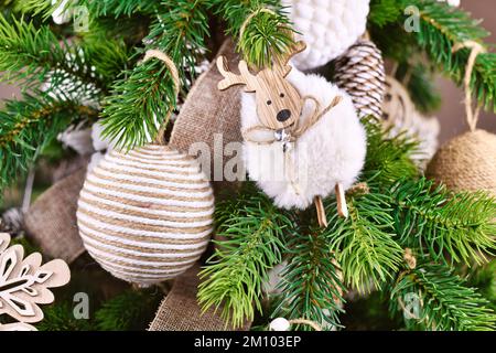 Natürliche Weihnachtsbaumschmuck aus beigefarbenem und weißem Juteseil und Schafsschmuck auf Baumzweigen Stockfoto