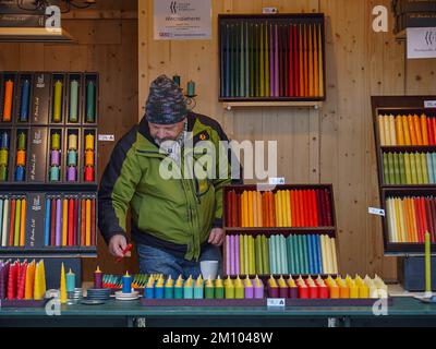 Ein Mann verkauft farbenfrohe Kerzen in einem Kiosk auf der Wiener Weihnachtsmesse. Blick auf den Weihnachtsmarkt mit einem Verkäufer, der Kerzen verkauft. Stockfoto