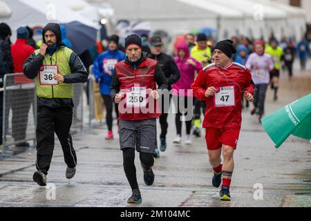 Sportler, die anlässlich des Telethon-Marathon-Staffelrennen unter Regen laufen. Udine City, Italien. 4. Dezember 2022. Stockfoto