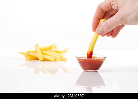 Tauchen Sie pommes frites von Hand in Ketchup, isoliert auf weißem Hintergrund Stockfoto